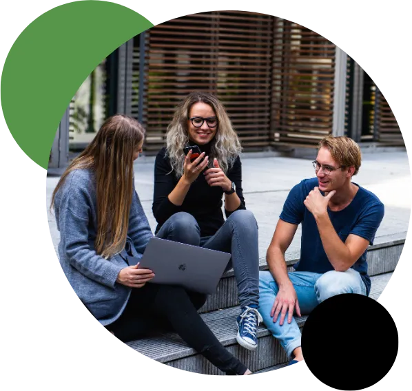 Detailed view of three young business professionals dressed casually, sitting together on concrete steps outdoors; a blonde woman holds a phone, another woman works on a laptop, and a man in a blue shirt smiles while participating in the strategy discussion.