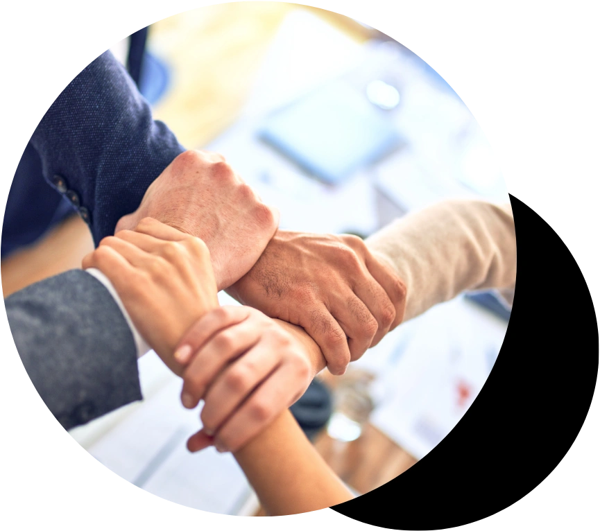 A close up overhead view of four business professionals crossing and interlocking their hands tightly over an office table, symbolizing corporate alignment, joint ventures, mutual trust, and strong team partnership.