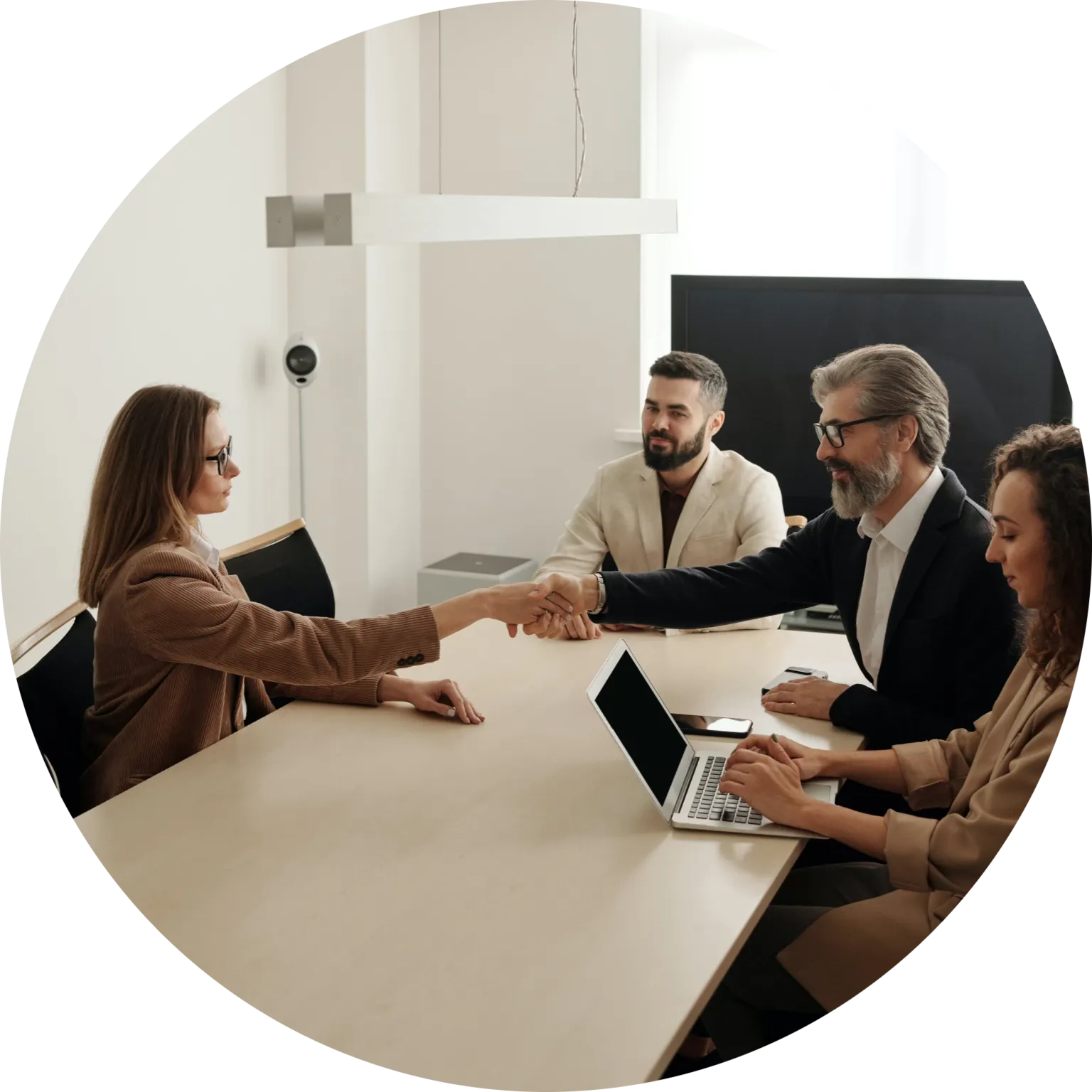 Detailed shot of a female professional in a brown blazer shaking hands across a conference room table with a bearded male colleague in a black suit jacket, while two other team members look on during a business funding consultation.